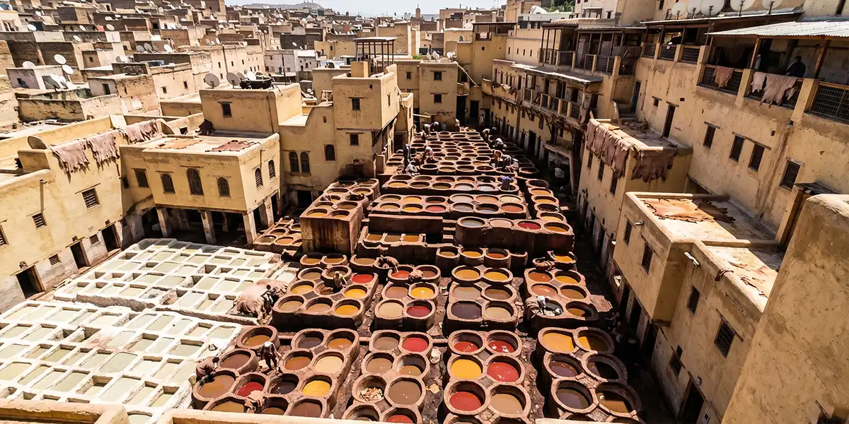 Overhead view of the Chouara tannery in Fez with circular dye vats in yellow, red and brown surrounded by medina rooftops